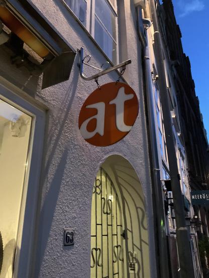 Shop sign for “at Fahrräder,” the letters “at” on an orange disk.