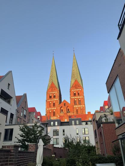 zwei von der untergehenden Sonne angestrahlte Backsteinkirchtürme (St. Marien) vor blauem Himmel 