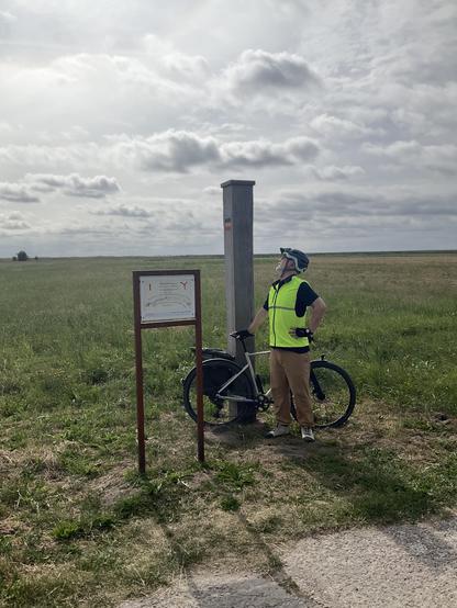 Grenzpfahl auf den Boddenwiesen, der Mann und sein Velo stehen davor, noch ein Erklärschild